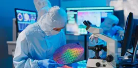 asian male technician in sterile coverall holds wafer that reflects many different colors with gloves and check it at semiconductor manufacturing plant